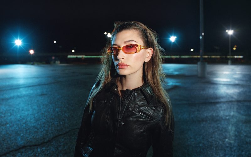 Donna con occhiali da sole Miu Miu rettangolari a lenti arancio, di notte in un parcheggio