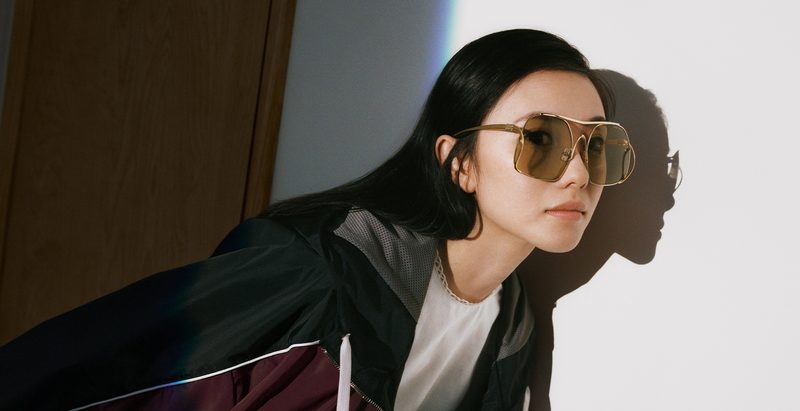 Donna con occhiali da sole Miu Miu in metallo davanti a una parete bianca