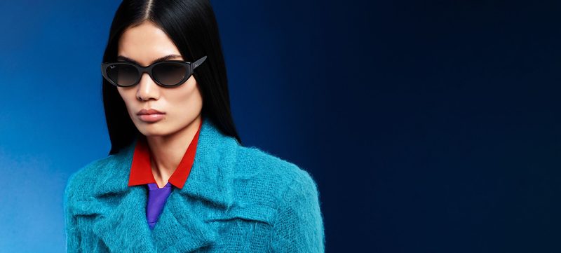 Donna con occhiali da sole Ray-Ban neri ovali e cappotto azzurro